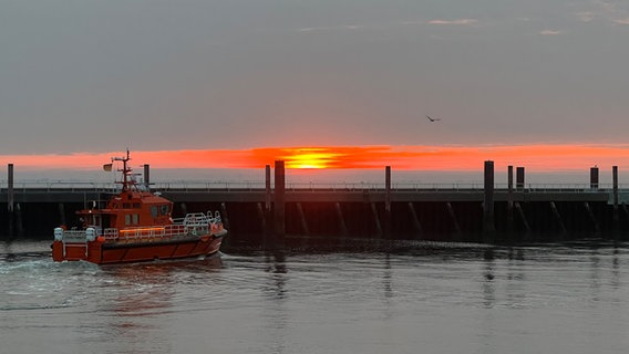 Roter Sonnenaufgang in Cuxhaven am ehemaligen Pier Alte LIebe. Im Vordergrund ein kleines Schiff. © NDR Foto: Manuela Heselhaus