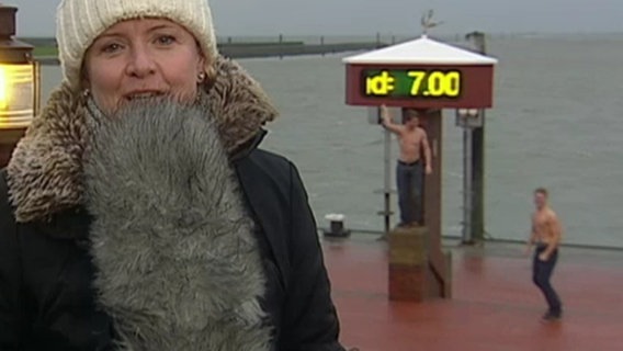 Hinter einer Moderatorin tanzen zwei Männer mit nacktem Oberkörper. Hinter einer Moderatorin tanzen zwei Männer mit nacktem Oberkörper. © tagesschau24