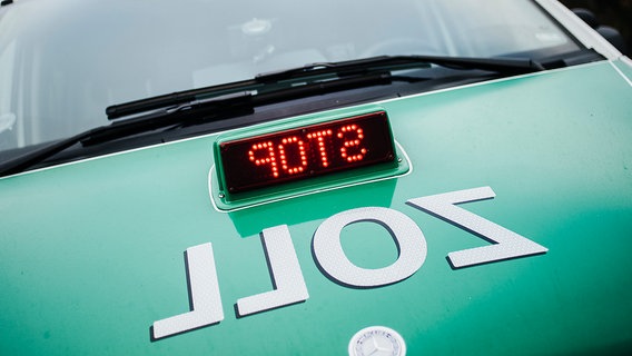 Auf der Motorhaube eines grünen Streifenwagens steht der Schriftzug Zoll und eine Leuchtanzeige zeigt das Wort Stop an. © NDR Foto: Julius Matuschik