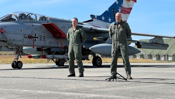 Mehrere Militärangehörige stehen vor Flugzeugen auf einem Rollfeld und sprechen in Mikrophone. Mehrere Militärangehörige stehen vor Flugzeugen auf einem Rollfeld und sprechen in Mikrophone. © NDR Foto: Jörg Jacobsen