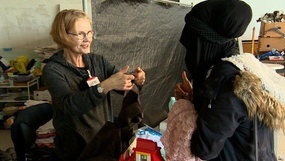 Eine ehrenamtliche Helferin versorgt eine Geflüchtete mit Kleidung. © NDR 