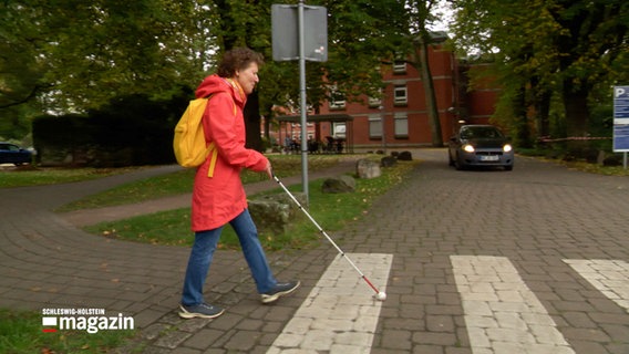 Ein Frau mit einem Blindenstock überqert einen Zebrastreifen. © NDR 