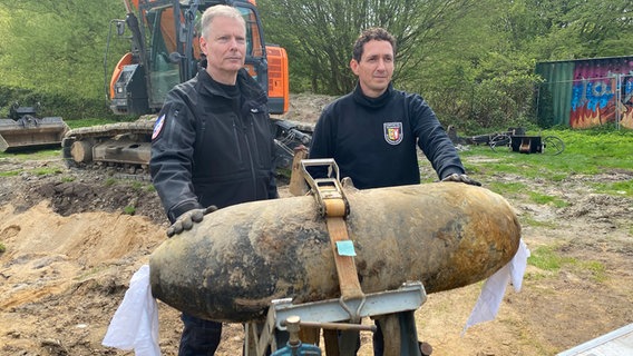 Oliver Kinast und Mirko Haack vom Kampfmittelräumdienst stehen hinter einer Bombe. © NDR Foto: Moritz Kodlin
