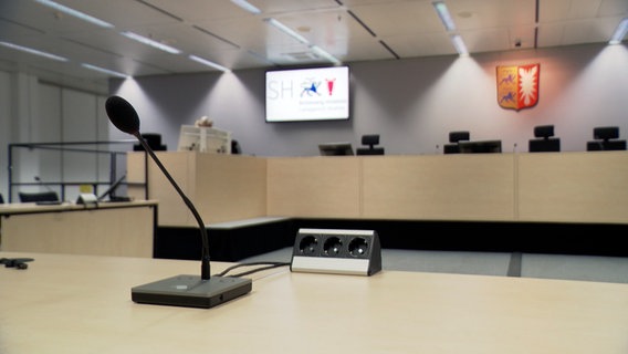 Ein Mikrofon steht auf einem Tisch in einem Gerichtssaal des Landgerichts Itzehoe. © NDR 