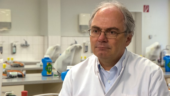 Virologe Dr. Helmut Fickenscher sitzt in einem Labor bei einem Interview. © NDR 
