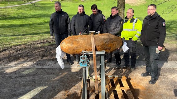 Menschen posieren um eine entschärfte Fliegerbombe aus dem zweiten Weltkrieg. © NDR Foto: Sofia Tchernomordik