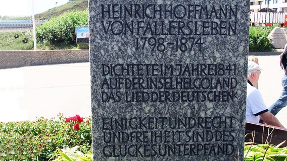 Eine Gedenktafel für Hoffmann von Fallersleben steht auf einer grün bepflanzten Fläche. © Kurverwaltung Helgoland Foto: Kurverwaltung Helgoland