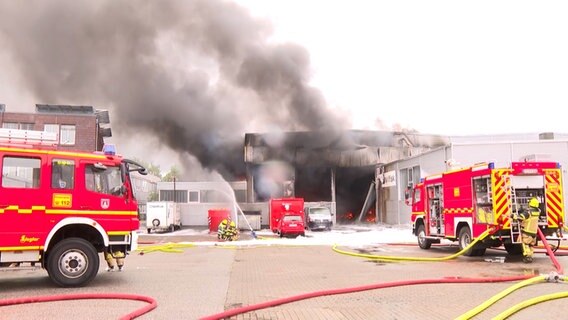 Einsatzkräfte der Feuerwehr löschen einen Brand in einer Lagerhalle.  