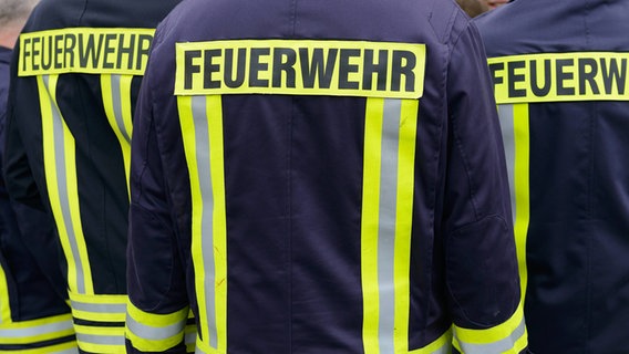 Drei Feuerwehrmänner in Uniform kehren ihren Rücken zur Kamera. © imago/penofoto Foto: imago/penofoto