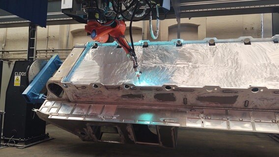 Ein großer Roboter schweißt an einer dicken Aluminiumhülle. © NDR Foto: Peer-Axel Kroeske