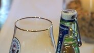 Eine Flasche mit dem Etikett Flensburger Wasser steht neben einem Bierglas auf einem Tisch in einem Konferenzraum der Flensburger Brauerei. © NDR 