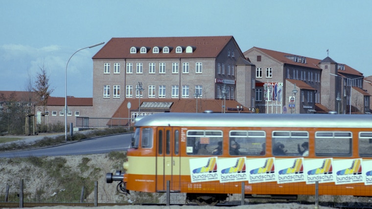 Im Hintergrund die Moorbekpassage Norderstedt um 1985, im Vordergrund fährt eine Straßenbahn durch das Bild. © Stadtarchiv Norderstedt Foto: Stadtarchiv Norderstedt