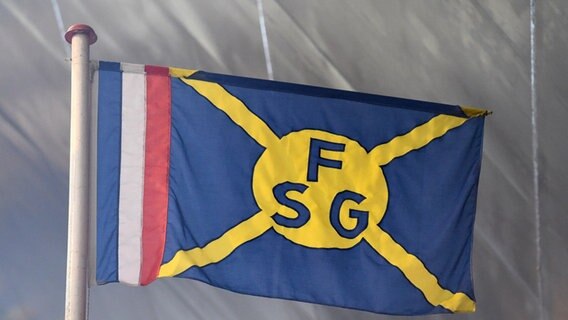 Eine FSG-Fahne weht in Flensburg auf dem Gelände der Flensburger Schiffbaugesellschaft. © dpa/picture alliance Foto: Carsten Rehder