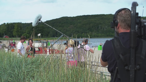Ein Kamerateam dreht mit Kamera und Tonangel am Strand mit zwei Menschen. © NDR Foto: Lena Storm