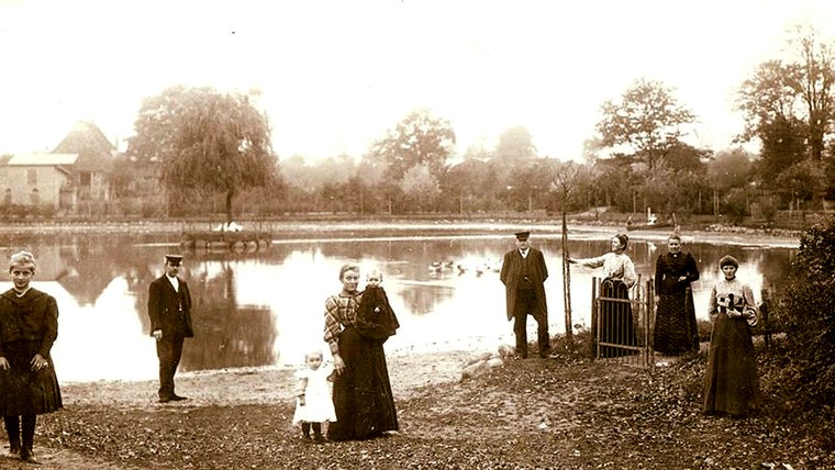 Der Wöddel in Henstedt-Ulzburg um 1900 herum. Eine Frau posiert mit ihren zwei Kindern vor einem flachen See. © Gemeindearchiv Henstedt-Ulzburg Foto: Gemeindearchiv Henstedt-Ulzburg