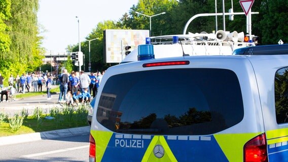 Hinter einem Polizeiauto laufen Holstein Kiel Fans in Richtung Stadion. © imago images / Lobeca Foto: imago images / Lobeca