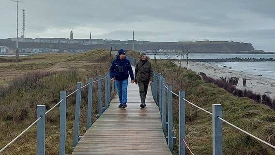 Zwei Menschen gehen über eine Dünenbrücke auf Helgoland. Zwei Menschen gehen über eine Dünenbrücke auf Helgoland. © NDR Foto: Laura Albus