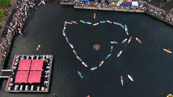 Menschen auf SUP-Boards bilden ein Herz auf dem Wasser um die Fördenixen im Flensburger Hafen beim NDR Sommer Festival. © NDR (Drohnen-Aufnahme) Foto: Peer-Axel Kroeske