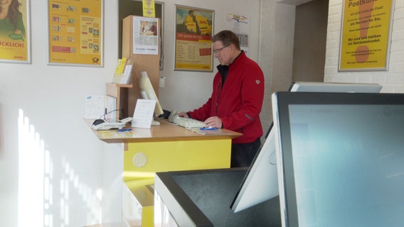 Ein Mann steht hinter einem Tresen eines Postshop © NDR Foto: NDR Screenshot
