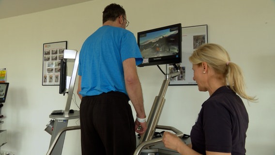 Ein Mann steht auf einem Gerät um sein Gleichgewicht zu trainieren, durch Gewichtsverlagerung wird auf einem Bildschirm ein virtueller Skiläufer gesteuert © NDR Foto: NDR Screenshot