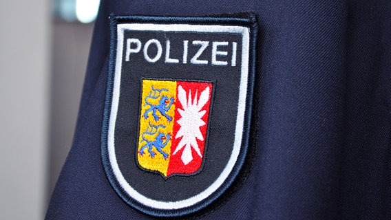 Auf dem Ärmel einer blauen Polizeiuniform ist das Polizeiwappen zu sehen. Über dem Wappen von Schleswig-Holstein steht in weißen Großbuchstaben Polizei geschrieben. © NDR Foto: Robert Holm