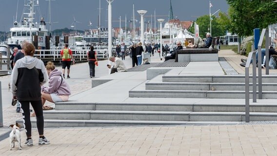 Einige Menschen sitzen auf hellen Stufen richtung Wasser, andere spazieren die Promenade entlang. © dpa-Bildfunk Foto: Markus Scholz