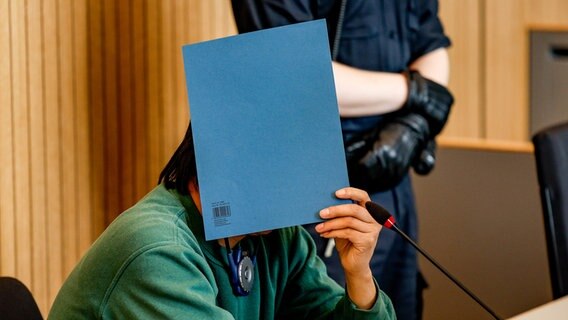 Der wegen Totschlags angeklagte 45-jährige Restaurantbesitzer versteckt sich vor Beginn der Verhandlung  hinter einem Ordner © dpa-Bildfunk Foto: Axel Heimken/dpa