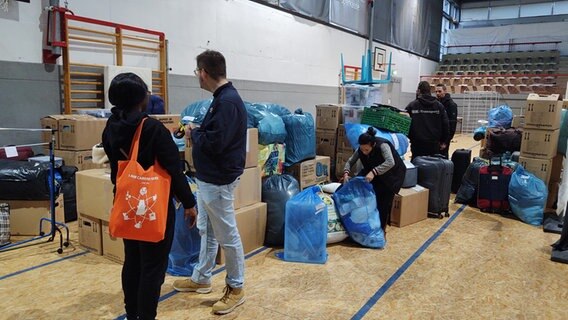 Menschen stehen vor einem Lager mit Umzugskartons in der Flensburger Fördehalle. © NDR Foto: Peer-Axel Kroeske