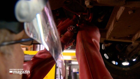 Ein Mechaniker arbeitet am Unterboden eines Elektroautos. © NDR 