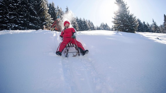 Kindern fahren mit ihren Schlitten einen Berg hinunter. © picture alliance / Westend61 Foto: Hans Huber