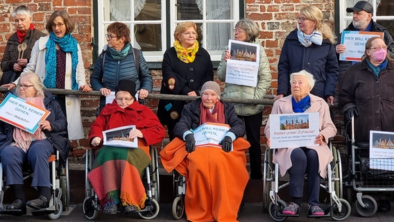 Bewohner sitzen in Rollstühlen vor dem Heiligen-Geist-Hospital, eingepackt in dicke Decken, halten Plakate hoch. Etwa 80 Senioren und Angehörige demonstrieren. © NDR Foto: Julian Marxen
