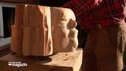 Eine Holzskulpture mit einem Gesicht steht auf einem Sockel © NDR 