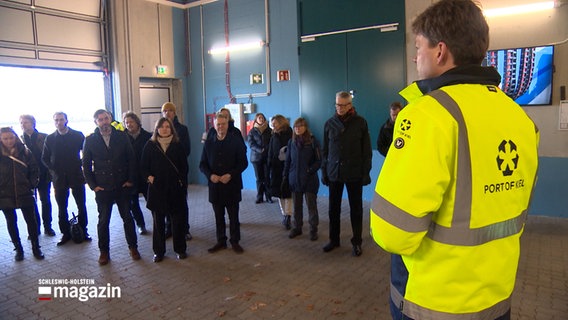 Eine Delegation steht im Halbkreis vor einem Mann in gelber Warnweste © NDR 