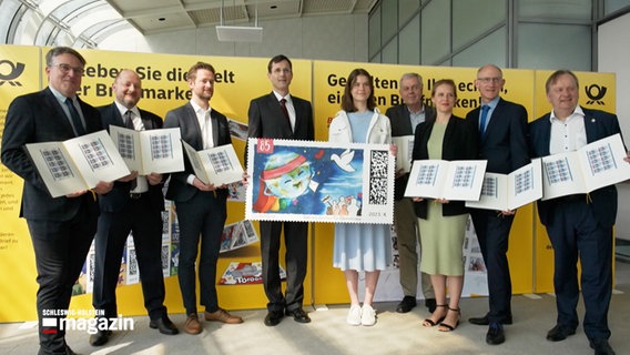 Schülerin Leonie Hansen steht bei der Preisverleichung für den Gestaltungswettbewerb der Deutschen Post mit einer überdimensionalen großen Briefmarke neben verschiedenen Männern und einer Frau © NDR 
