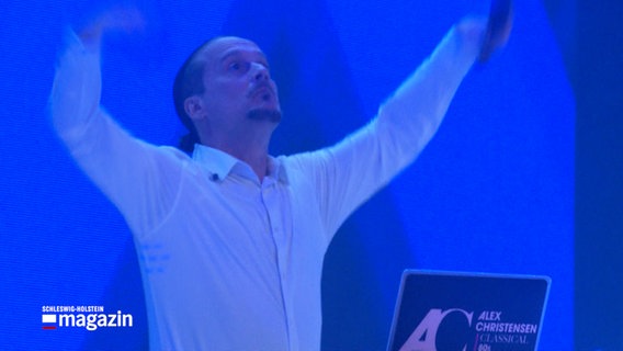 Der Musikproduzent und DJ Alex Christensen steht während eines Konzertes auf einer Bühne © NDR Foto: NDR Screenshot