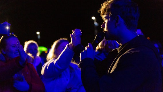 Sänger Moritz Garth hält die Hand einer Zuschauerin vor der NDR-Bühne im Rahmen des Abendprogramms des SH Netz Cup. © NDR Foto: Anna-Lena Storm