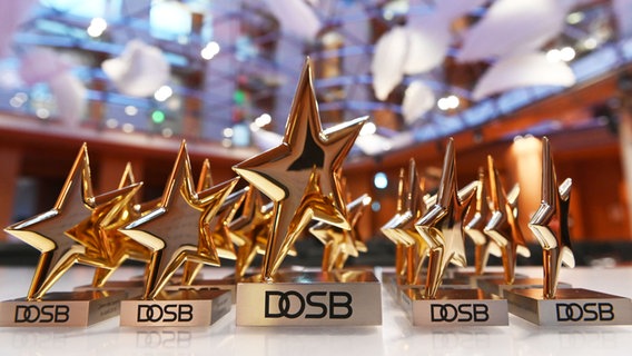 Mehrere goldene Sterne auf Sockeln mit dem Schriftzeug "DOSB" stehen aufgereiht hintereinander.  Foto:  Frank May, Gerald Matzka