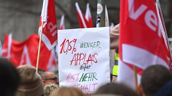 Zwischen Fahnen der Gewerkschaft verdi wird ein Schild hochgehalten, auf dem steht: 10,5 Prozent weniger Applaus dafür 10,5 Prozent mehr Gehalt. © Imago Images / Sven Simon Foto: Sven Simon