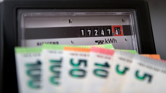 Euro-Geldschein werden vor einem Stromzähler im Privathaushalt gehalten. © IMAGO / MiS 