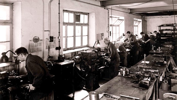 Eine alte Schwarz-weiß-Fotografie zeigt mehrere Männer an Maschinen in der Werkstatt © Lutz Bertram Foto: Lutz Bertram