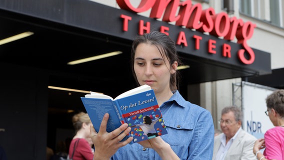 Eine junge Frau liest ein Buch vor dem Eingang des Ohnsorg Theaters in Hamburg. © NDR Foto: Oke Jens