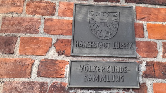 Ein Metallschild an einer Hauswand weist auf die Völkerkundesammlung in Lübeck hin. © Völkerkundesammlung Lübeck Foto: Dr. Lars Frühsorge