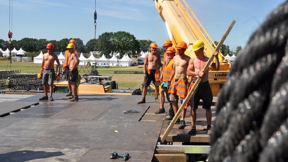 Bauarbeiter mit nackten Oberkörpern bauen den Fußboden einer Bühne auf dem Festival-Gelände in Wacken auf. © NDR Foto: Eva Schulze-Gabrechten
