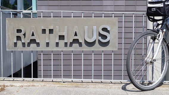 An einem Zaun ist ein Betonschild mit der Aufschrift "Rathaus" befästigt. Daneben steht ein Fahrrad. © NDR Foto: Jörg Jacobsen