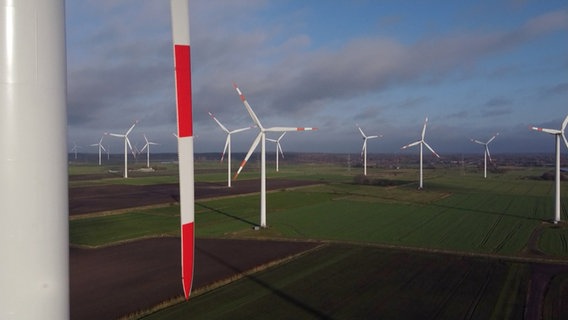 Zahlreiche Windräder mit Rot-Weißen Rotorblättern stehen auf offener Fläche. © NDR 