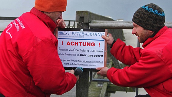 Mitarbeiter der Tourismuszentrale befestigen ein Warnschild an der Seebrücke in St. Peter-Ording © dpa Foto: Wolfgang Runge