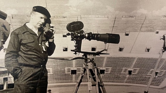 Eine schwarzweiß Aufnahme zeigt einen Mann neben einer Kamera stehend mit einem Feldtelefon in der Hand. © Hilde Garms 