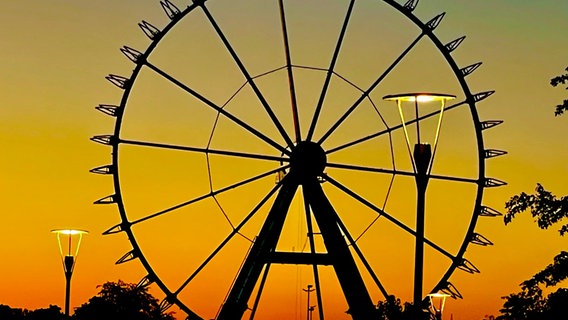 Die Sonne geht hinter einem Riesenrad auf dem Kramermarkt unter. © NDR Foto: Petra Olliges