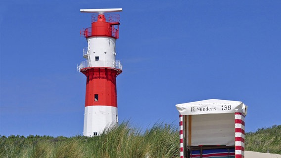 Ein Leuchtturm in den Dünen mit einem Strandkorb davor. © NDR 