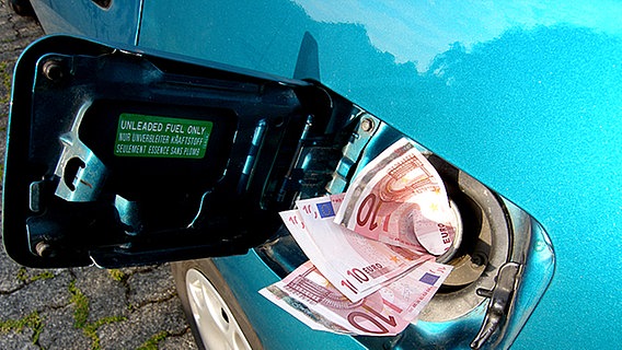 Ein Fächer Geldscheine verschwindet im Tank eines Autos. © picture-alliance 